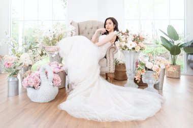 Göz kamaştırıcı bir gelinlik giymiş bir gelin, parlak bir odada çiçeklerin arasında bir anın tadını çıkarır..