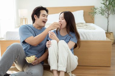 Genç bir çift, sıcak yatak odalarının zemininde dinlenirken patlamış mısır paylaşır ve gülümser..