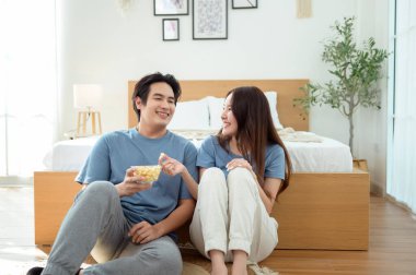 Genç bir çift, sıcak yatak odalarının zemininde dinlenirken patlamış mısır paylaşır ve gülümser..