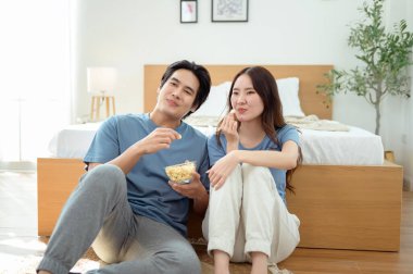 Genç bir çift, sıcak yatak odalarının zemininde dinlenirken patlamış mısır paylaşır ve gülümser..