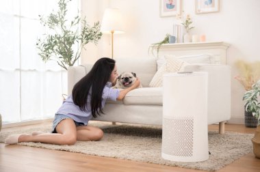 Parlak bir odada, şık bir kanepenin yanında köpeğini okşayan bir kadın gülümsüyor..