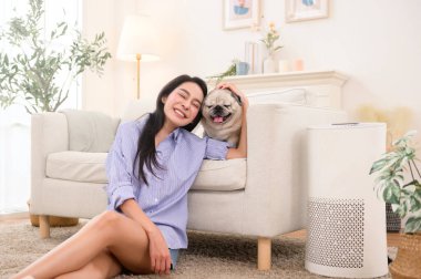 Parlak bir odada, şık bir kanepenin yanında köpeğini okşayan bir kadın gülümsüyor..