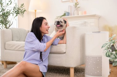 Parlak bir odada, şık bir kanepenin yanında köpeğini okşayan bir kadın gülümsüyor..