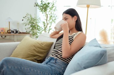 Genç Asyalı kadın evde kahve içmekten zevk alıyor.