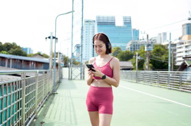 Bir kadın şehir yolunda koşar, telefonunu kontrol ederken gülümser ve müzik dinler..