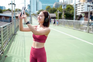 Bir kadın şehir yolunda koşar, telefonunu kontrol ederken gülümser ve müzik dinler..