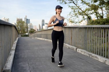 Bir kadın sabahın erken saatlerinde şehir binalarıyla modern bir köprüde koşuyor..