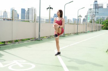 Aktif kıyafetli bir kadın şehir parkında güneşin tadını çıkarırken kollarını uzatıyor..