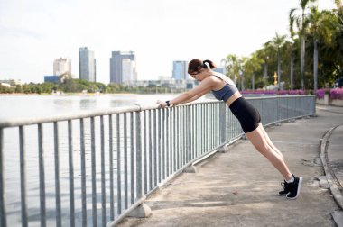 Bir kadın, şehir parkındaki bir rıhtımda esneme egzersizi yapıyor..