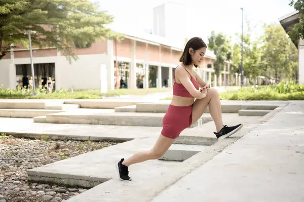 Bir kadın parkta esneme egzersizi yapıyor, güneş ışığı altında bacak kaslarına odaklanıyor..