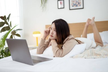 Genç Asyalı kadın yatak odasında dizüstü bilgisayar kullanmaktan zevk alıyor.