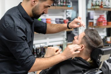 barber makes eyebrow correction for a man in the salon with a thread