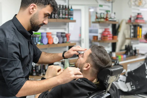 barber makes eyebrow correction for a man in the salon with a thread