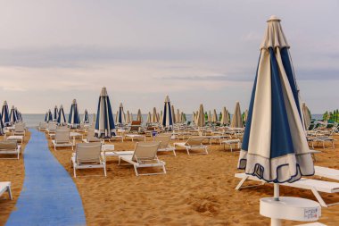 Sabah, deniz kenarında, boş güneş şezlongları, sandalyeler ve kumsalda kilitli şemsiyeler..