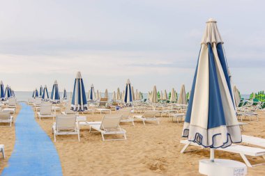 Sabah, deniz kenarında, boş güneş şezlongları, sandalyeler ve kumsalda kilitli şemsiyeler..