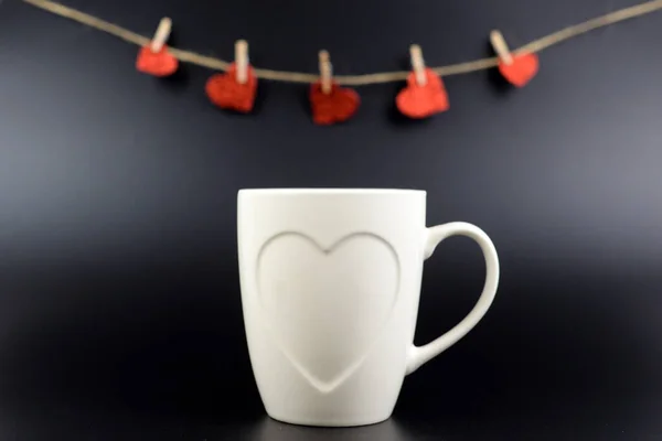 white cup of tea with hearts and hearts on a string on a black background, selective focus, copy space. Love concept.