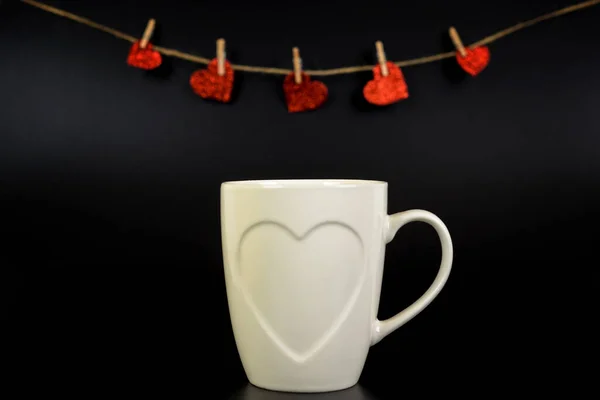 white cup of tea with hearts and hearts on a string on a black background, selective focus, copy space. Love concept.