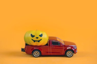  Kırmızı oyuncak araba ve turuncu balkabağı, turuncu arka planda çatıda. Çatıda küçük Cadılar Bayramı balkabakları olan eski model kırmızı bir oyuncak araba..