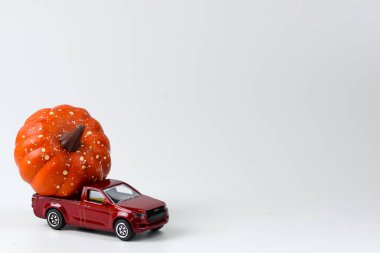Almanya, Heidelberg - 13 Eylül 2023: Beyaz arka planda kırmızı oyuncak araba ve turuncu balkabağı. Çatıda küçük Cadılar Bayramı balkabakları olan eski model kırmızı bir oyuncak araba..