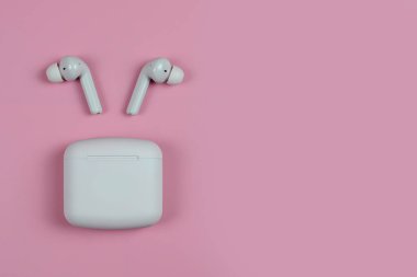 Düz depolama konsepti: kulaklıklar ve pastel renkli arka planda akıllı telefon. Pembe gri arkaplanda kablosuz kulaklıklar, üst görünüm, kopyalama alanı.