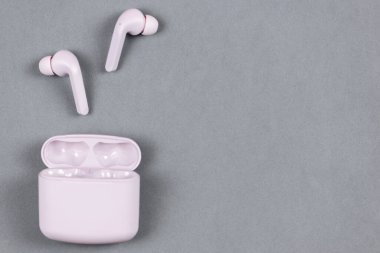 Düz depolama konsepti: kulaklıklar ve pastel renkli arka planda akıllı telefon. Pembe gri arkaplanda kablosuz kulaklıklar, üst görünüm, kopyalama alanı.