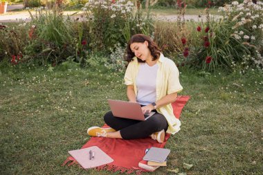 Dizüstü bilgisayarı olan ve parkta kitap okuyan genç bir kadın. Yüksek kalite fotoğraf