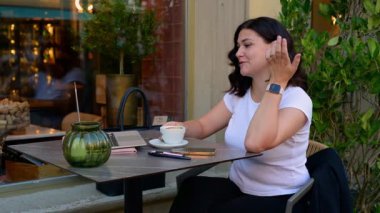 Video görüşmesi, dizüstü bilgisayar ve kafede uzaktan çalışma olanakları, komik şakalar ya da sanal toplantı hakkında gülen kız. Kafedeki röportajda konuşan mutlu bir kadın, girişimci ya da serbest çalışan. FullHD görüntüleri.