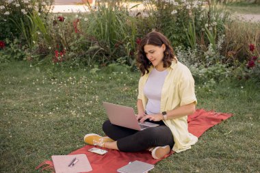 Dizüstü bilgisayarı olan ve parkta kitap okuyan genç bir kadın. Yüksek kalite fotoğraf