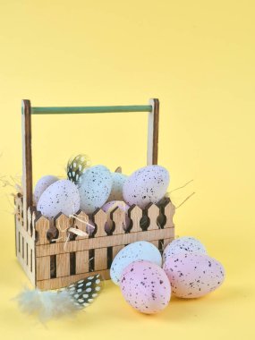 Colored quail eggs in basket on yellow background, Easter, vertical photo. High quality photo clipart