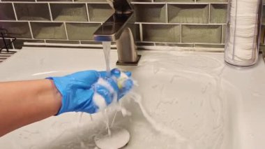 Lastik eldivenli bir elin yakın çekimi banyodaki musluğu yıkar. Yüzü olmayan. Yüksek kaliteli FullHD görüntüler