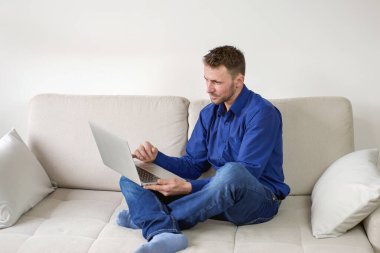 Evinden bilgisayar başında çalışan genç bir adam. Parlak, rahat bir oda, eğitim ve iş. Yüksek kalite fotoğraf