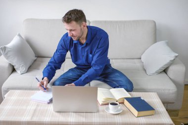 Evinden bilgisayar başında çalışan genç bir adam. Parlak, rahat bir oda, eğitim ve iş. Yüksek kalite fotoğraf