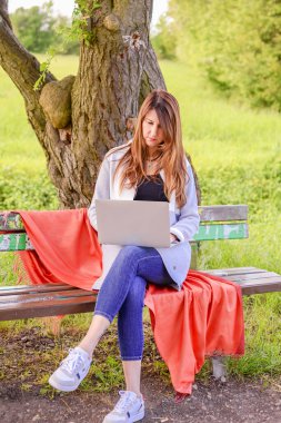 Yeşil bir çayırda dizüstü bilgisayarla oturan genç ve güzel bir kadının portresi..