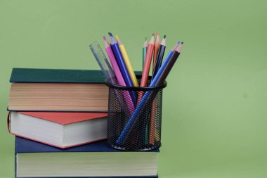 Renkli kalemlerle dolu canlı bir bardağın yanına düzgünce düzenlenmiş çeşitli kitaplar konur.