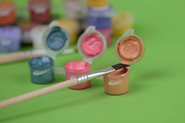 Renkli boyalarla dolu bir kovanın yanında bir boya fırçası var. Sanatsal dokunuşunu bekleyen yaratıcı projeler için hazır.