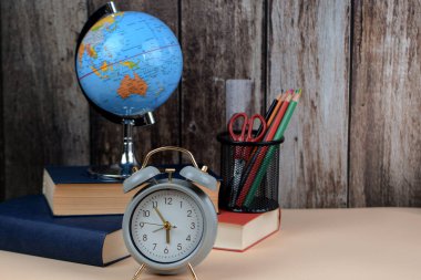 Bir kürenin ve bazı kitapların yanında duran bir masanın üzerinde duran çalar saat güzel bir natürmort düzeneği oluşturuyor.