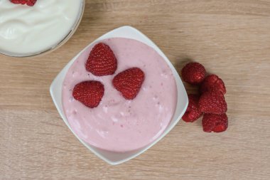 Lezzetli bir kase kremalı yoğurtla dolu ve üstünde taze ahudutlarla süslenmiş, kırsal ahşap bir masaya güzelce yerleştirilmiş.