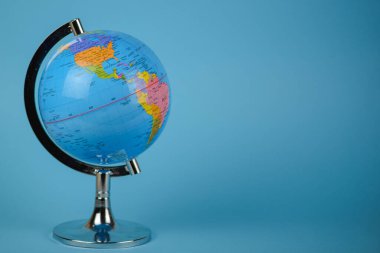 Gezegenimizi temsil eden küçük, detaylı bir küre parlak bir mavi masada duruyor ve sahneye biraz renk ve ilgi katıyor.