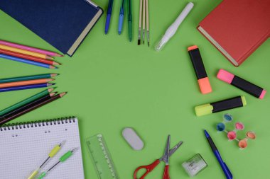 Çeşitli eğitim faaliyetleri ve ihtiyaçlar için çok çeşitli temel okul malzemeleriyle dolu canlı yeşil bir masa.