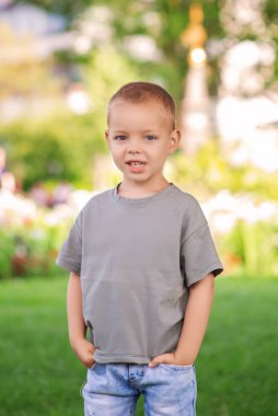 Neşeli genç bir çocuk neşeli bir bahçede neşeli bir şekilde poz verir, tasasız çocukluğun birçok neşesini gösterir.