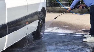Bir adam en uygun sonuç için güçlü bir basınç makinesiyle minibüsü iyice temizliyor.