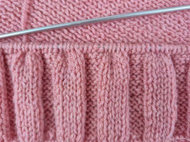 Pembe örgü yapılıyor. Örgü iğneleri ve düzgün döngüler desenli bir şablon oluşturuyor. Yumuşak yün yumağı sıcak bir atmosfer yaratıyor. El sanatları, yaratıcılık, örgü ve hobilerin teması. 