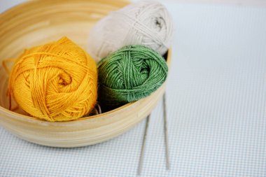 Üç canlı iplik topu dekoratif bir kasede dinleniyor. Bitmek bilmeyen el işi ve örgü projeleri için mükemmel.