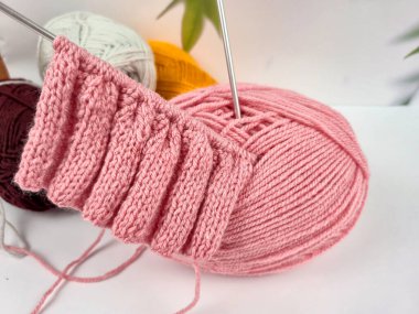 Pembe örgü yapılıyor. Örgü iğneleri ve düzgün döngüler desenli bir şablon oluşturuyor. Yumuşak yün yumağı sıcak bir atmosfer yaratıyor. El sanatları, yaratıcılık, örgü ve hobilerin teması. 