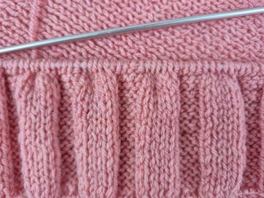 Pembe örgü yapılıyor. Örgü iğneleri ve düzgün döngüler desenli bir şablon oluşturuyor. Yumuşak yün yumağı sıcak bir atmosfer yaratıyor. El sanatları, yaratıcılık, örgü ve hobilerin teması. 