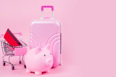 Pembe bir bavul, kumbara ve alışveriş arabasının yer aldığı canlı bir kurgu, seyahat tasarruflarını simgeliyor..