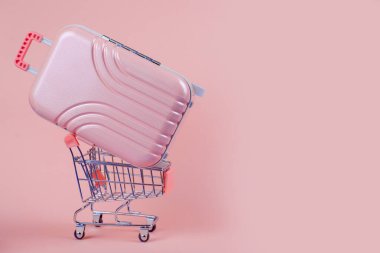 Moda ve modaya uygun pembe bir bavul, yumuşak bir pastel zemine karşı bir alışveriş arabasında rahatça dinleniyor.