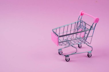 Şık ve şık bir mini alışveriş arabası canlı, pembe bir arka plana karşı, çeşitli perakende temaları için ideal.