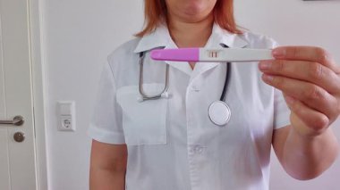 Doktor, beyaz arka planda pozitif hamilelik testi gösteriyor.