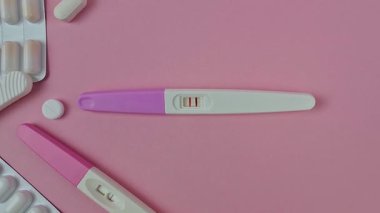 Pembe arka planda iki şeritli hamilelik testi